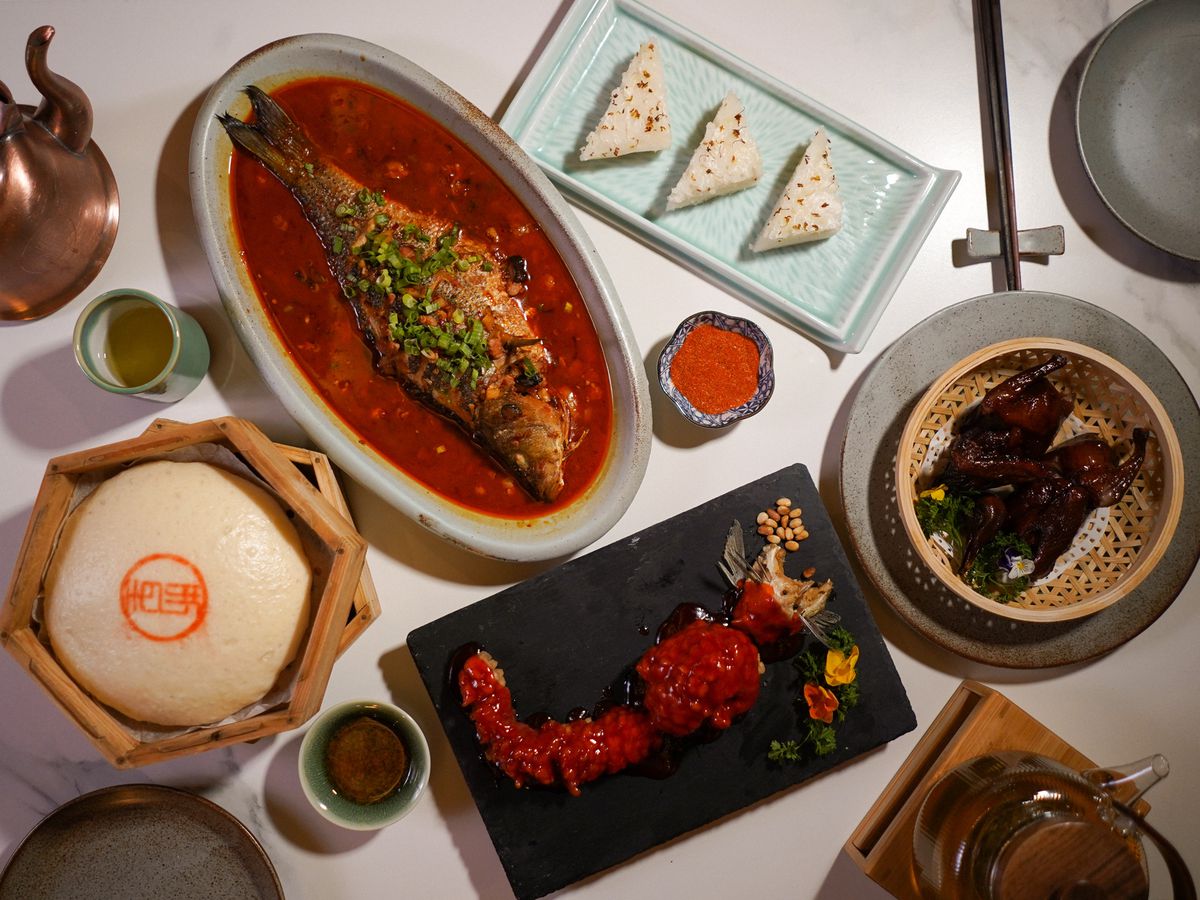 A spread of Shanghainese dishes, including whole fish, triangles of rice balls, lobster tail, quail, and a large mantou bun.