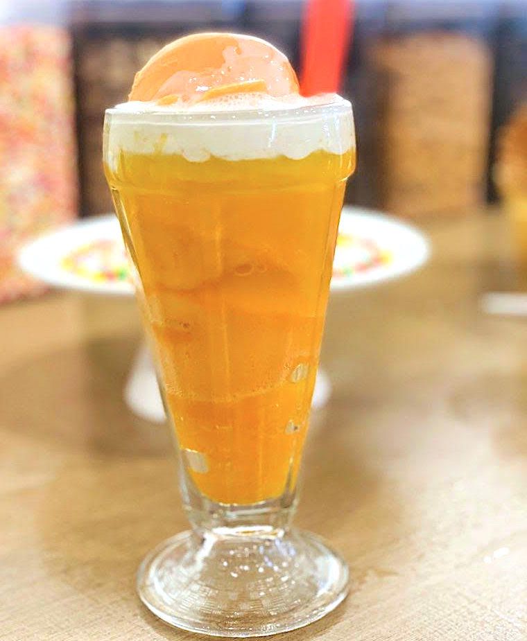 A classic ice cream glass tulip container filled with a bright orange mix topped with a frothy head
