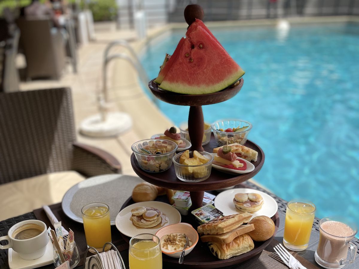 A tower of brunch items topped with a slice of watermelon, overlooking a pool. 