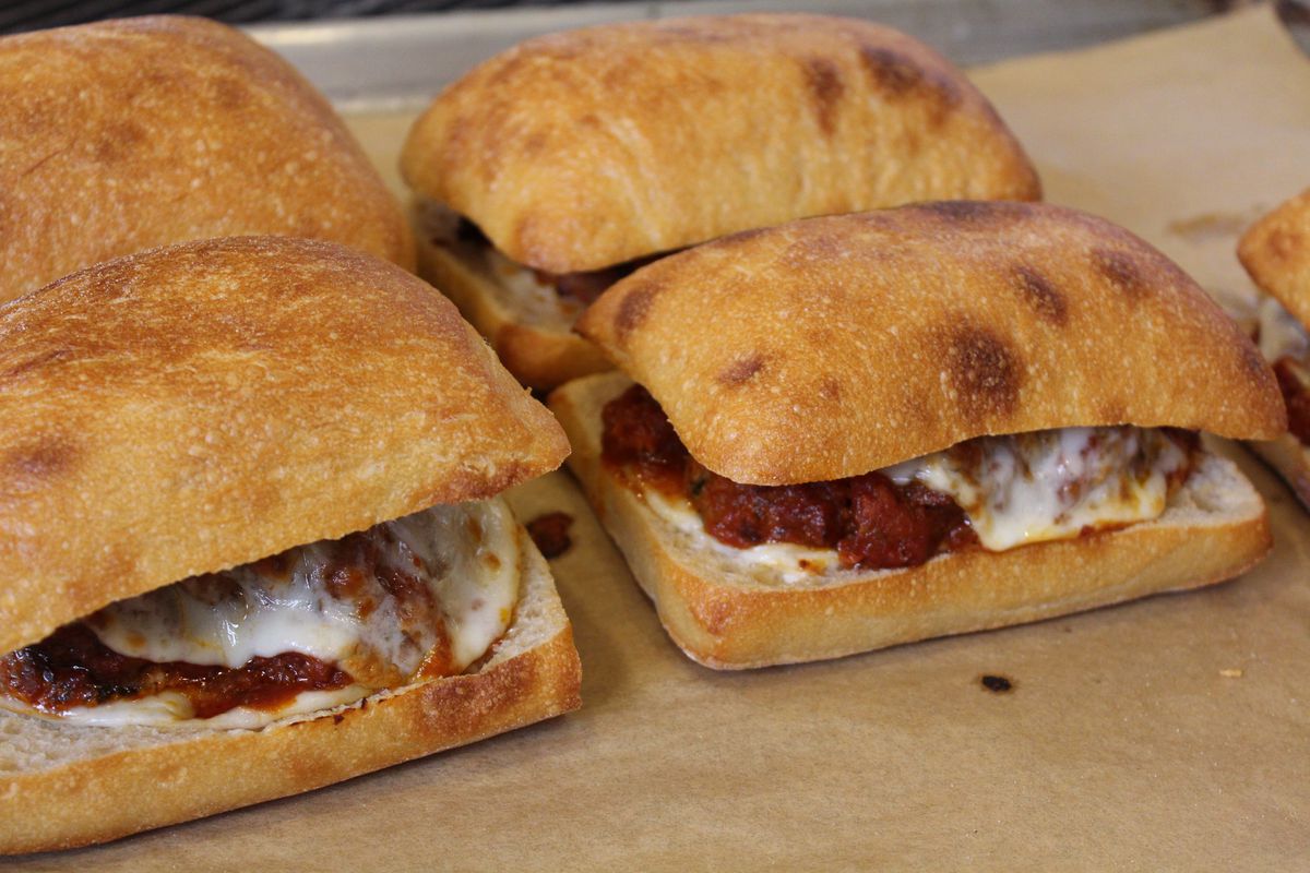 Four meatball sandwiches, oozing with melted white cheese