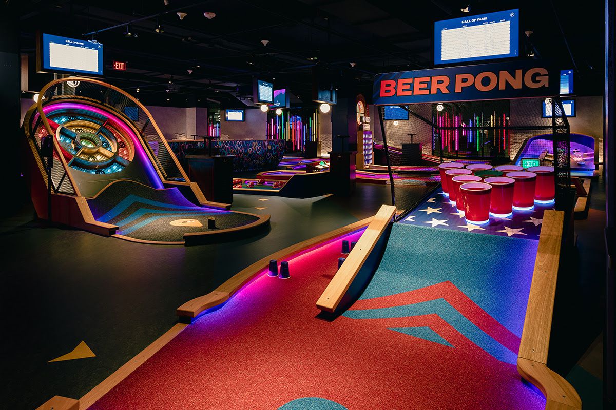 Interior view of an indoor mini golf course. The hole in the foreground is a giant beer pong setup.