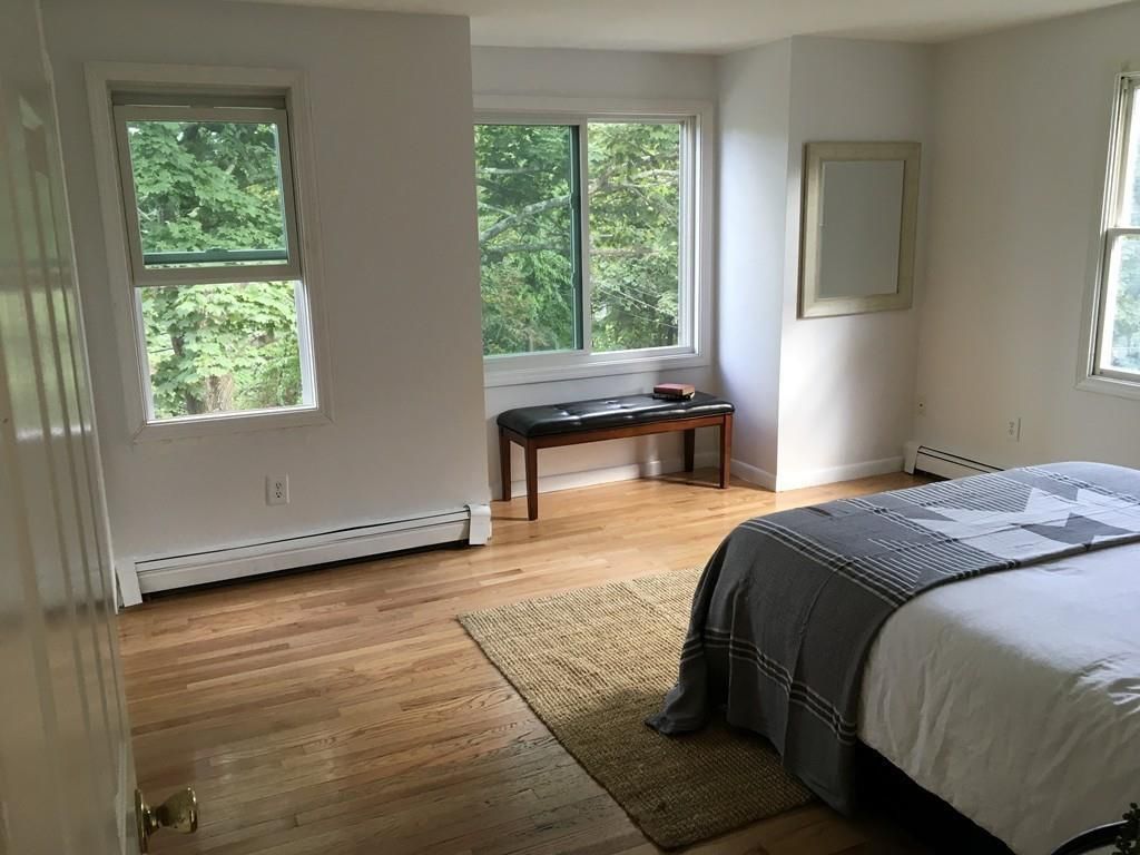 A bedroom with a bed, a bench, and large windows. 