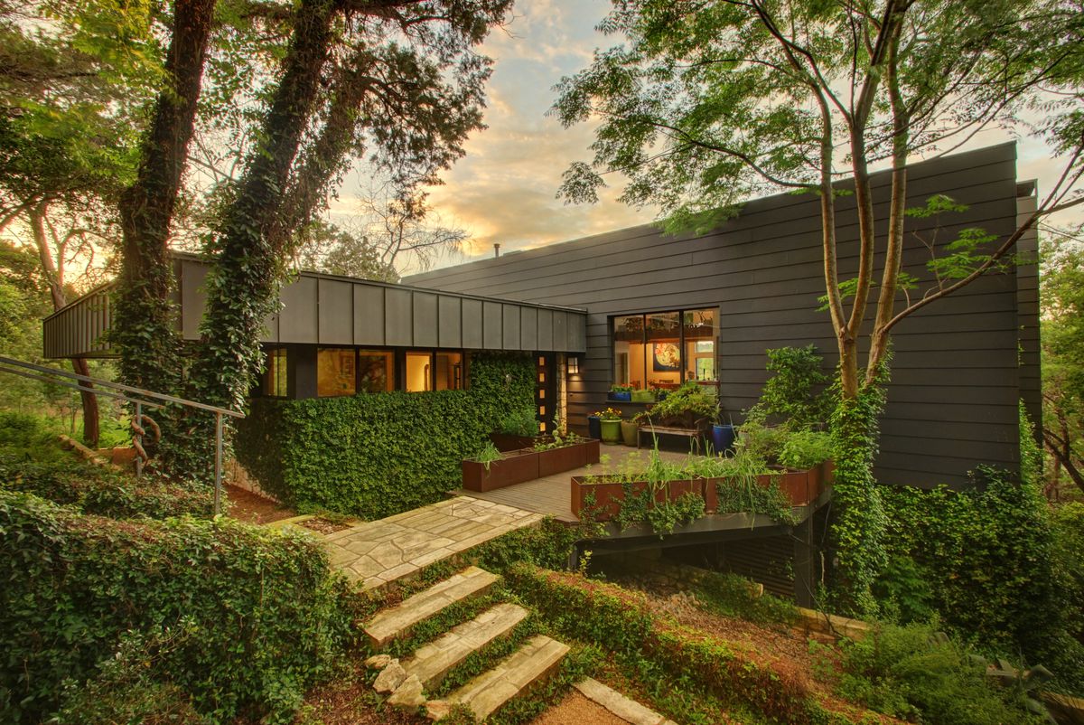 1992 boxy gray-brown metal one-story house with big patio, surrounded by very green forest