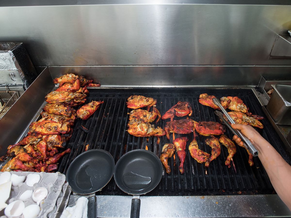 A black grill as a hand reaches in to turn blackened chicken.