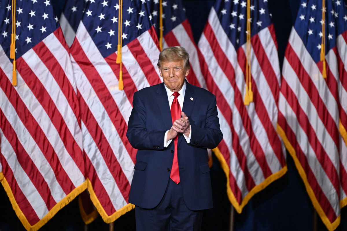 Trump stands in front of a background of American flags.