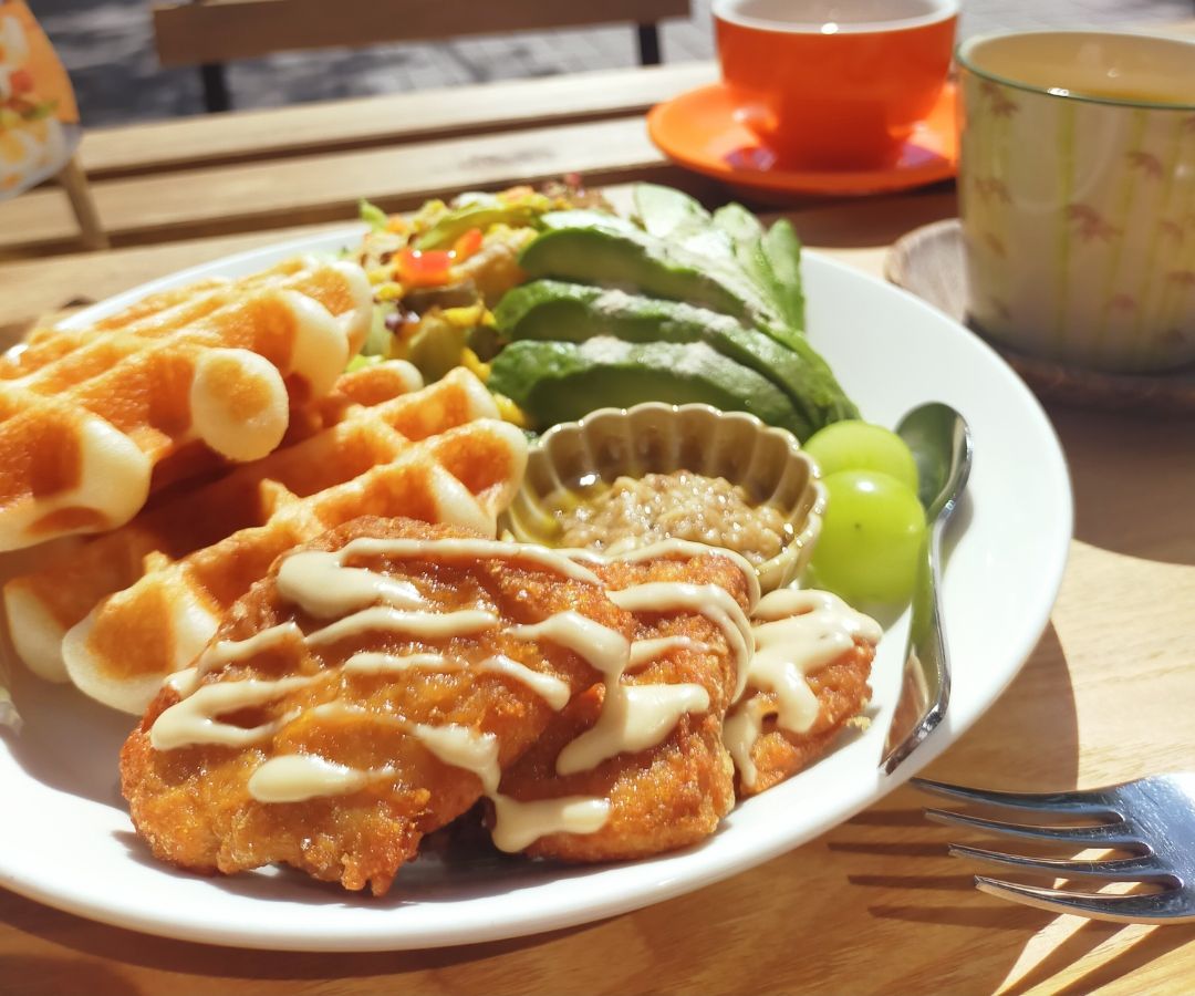 A mixed plate featuring waffles, avocado, and other items on a sunny patio table.