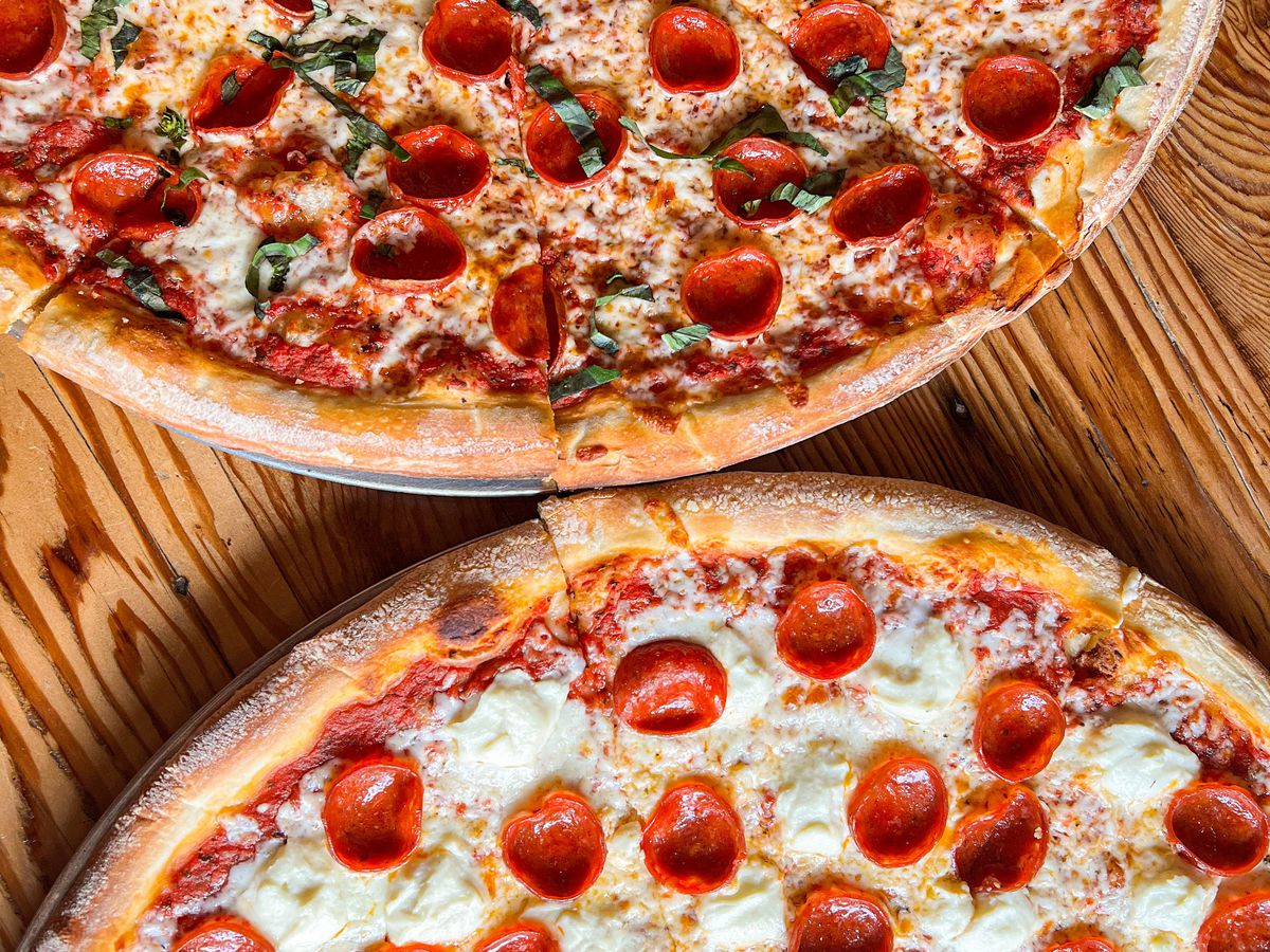 An overhead shot of two rounds of pizza, both with pepperoni, on a wooden table.