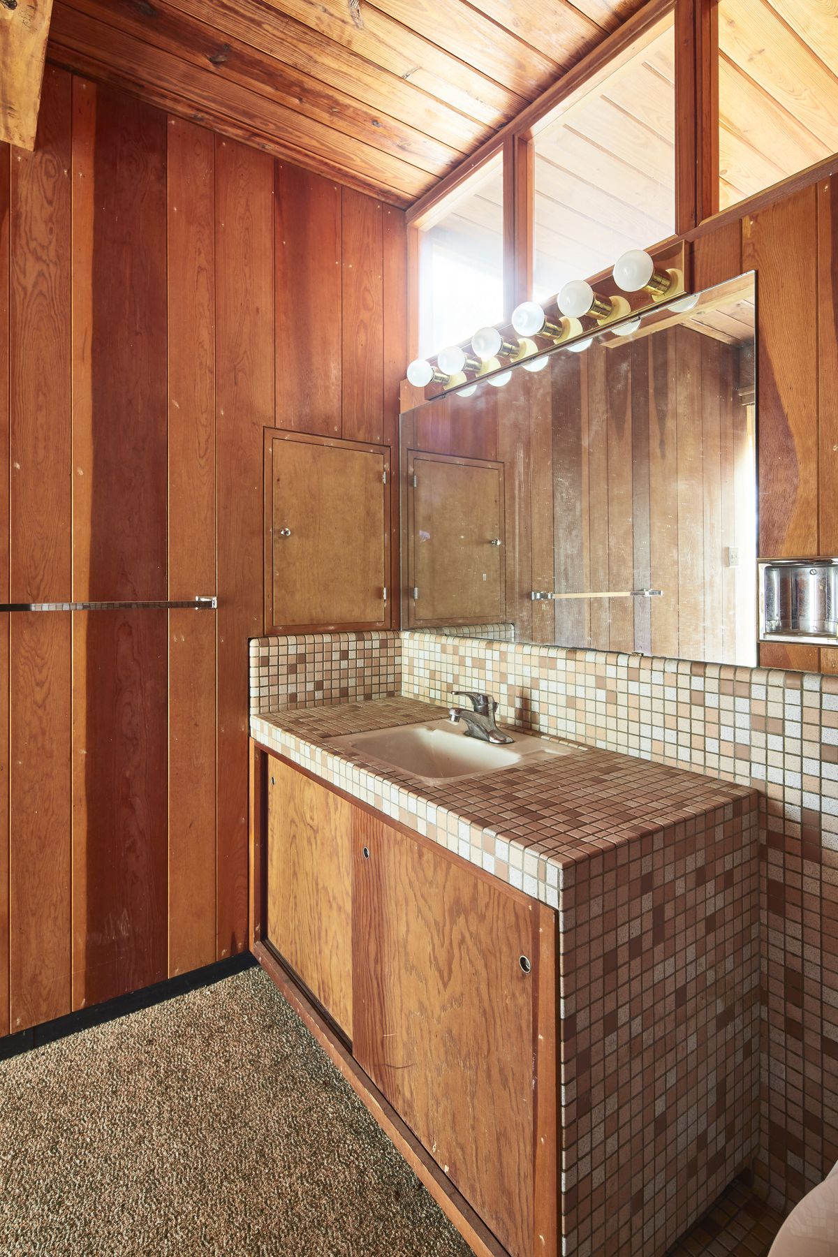 A bathroom with warm wood walls and cabinets, and small tiles.