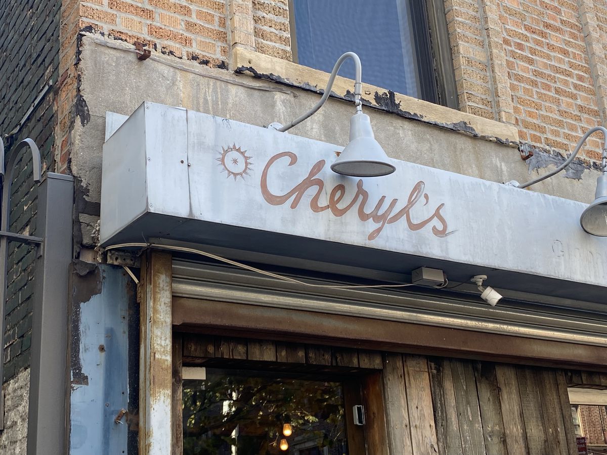 A faded grey sign is decorated with the word “Cheryl’s” in faded red paint.