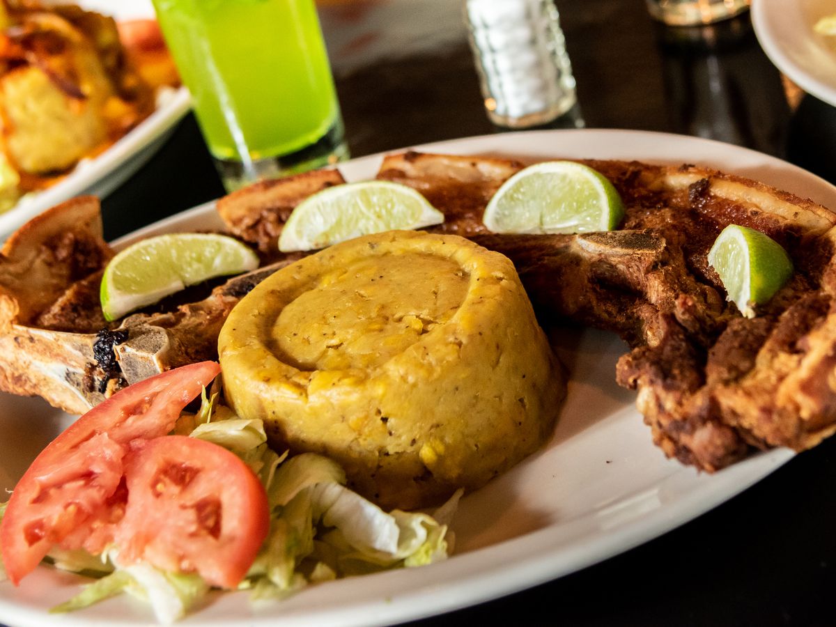 A long pork chop, topped with lime wedges, surrounding a mound of mofongo, with a side salad.