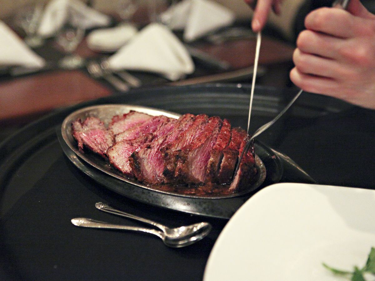 A steak in a silver dish being sliced with a knife and fork. 