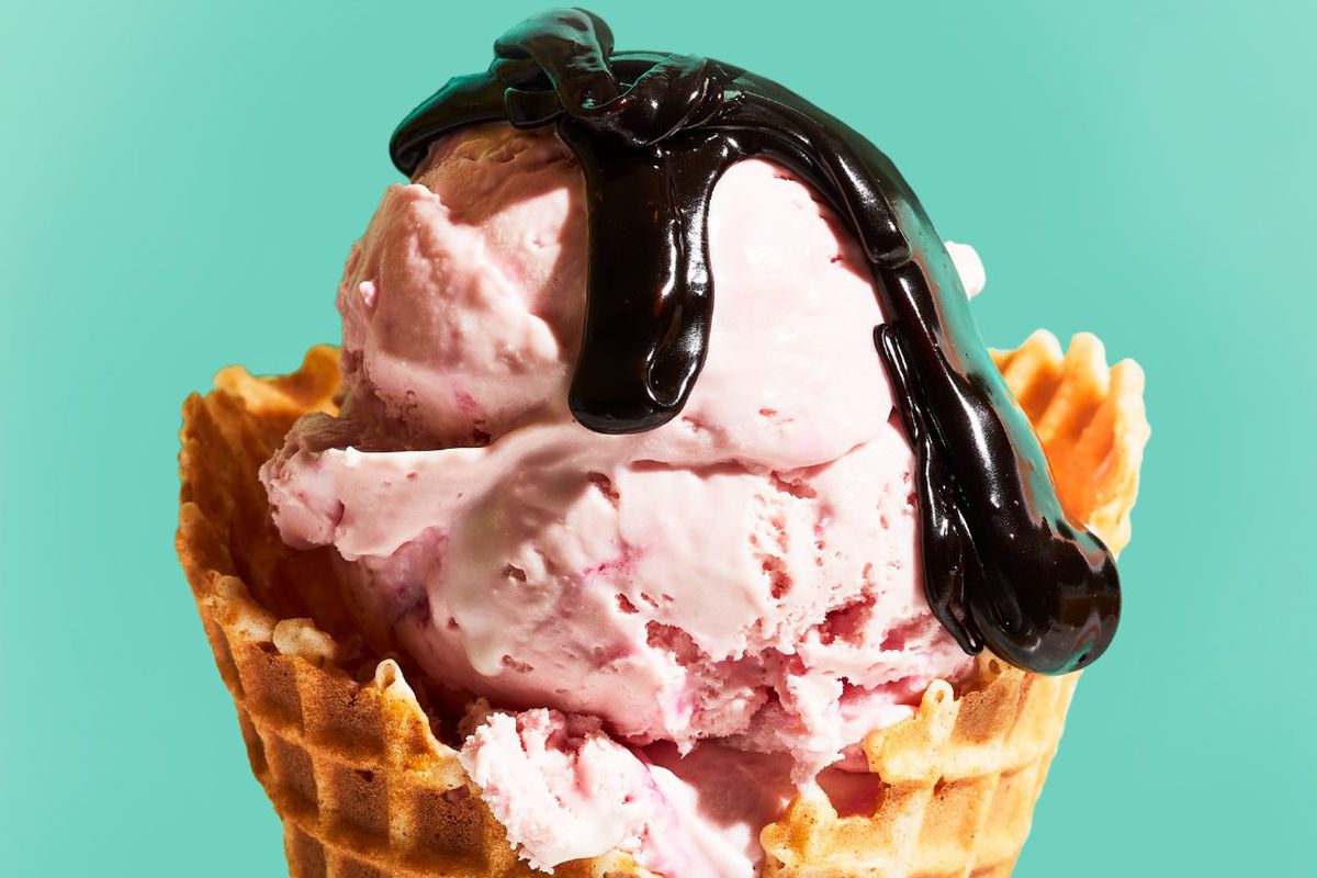 a scoop of pink ice cream in a waffle cone with a drizzle of chocolate syrup.