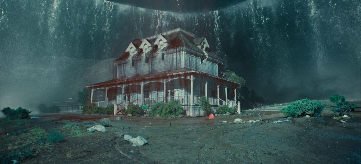 A farmhouse dripping with blood and viscera under the shadow of an ominous circular object raining down water in Nope.