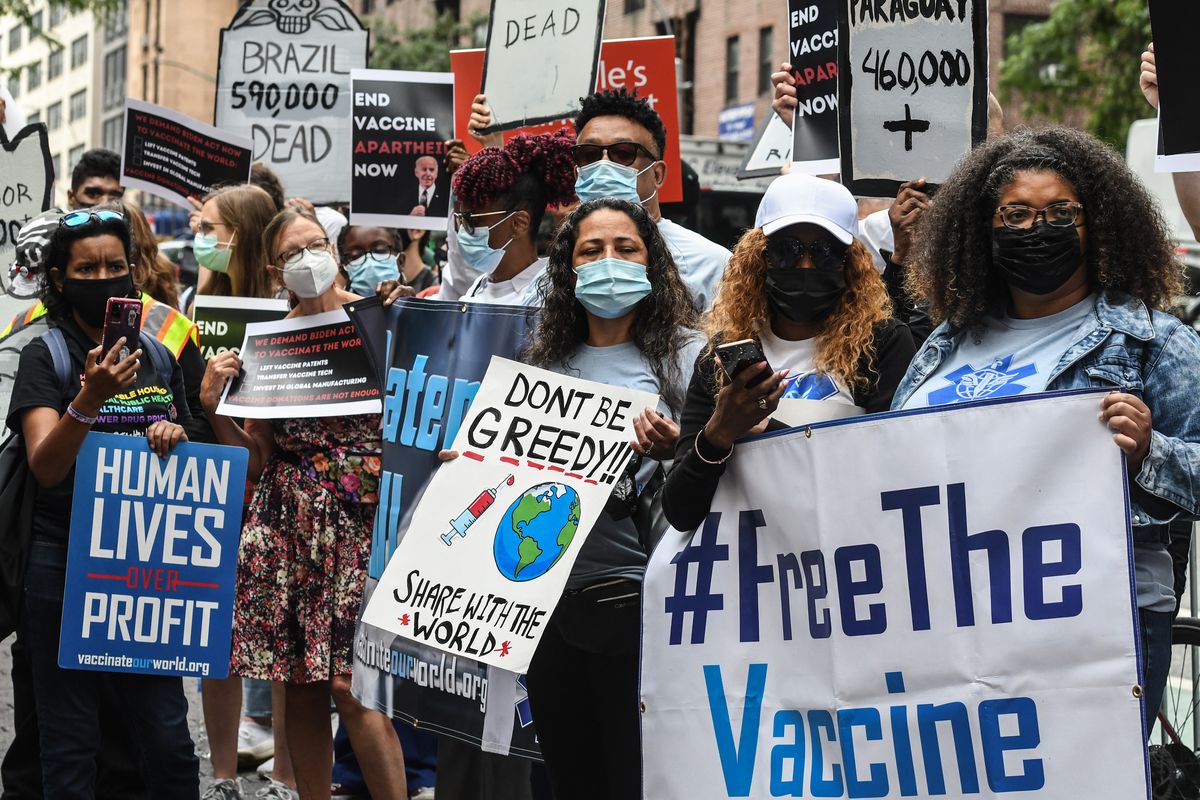 Protesters carry signs that read “Free the vaccine,” “Don’t be greedy, share with the world,” and “Human lives over profit.”