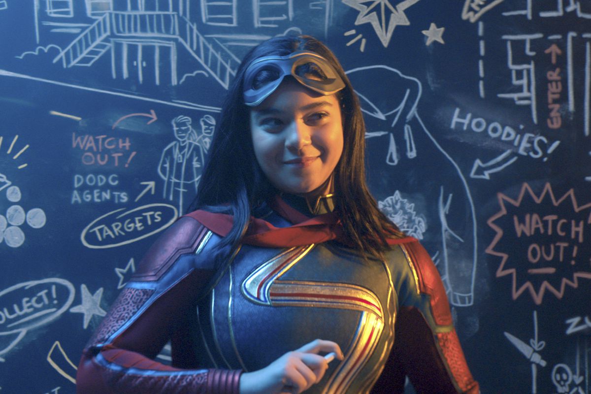 Kamala Khan/Ms. Marvel stands in front of a crowded chalkboard, smirking and holding a piece of chalk. Her mask is pushed up onto her forehead. 
