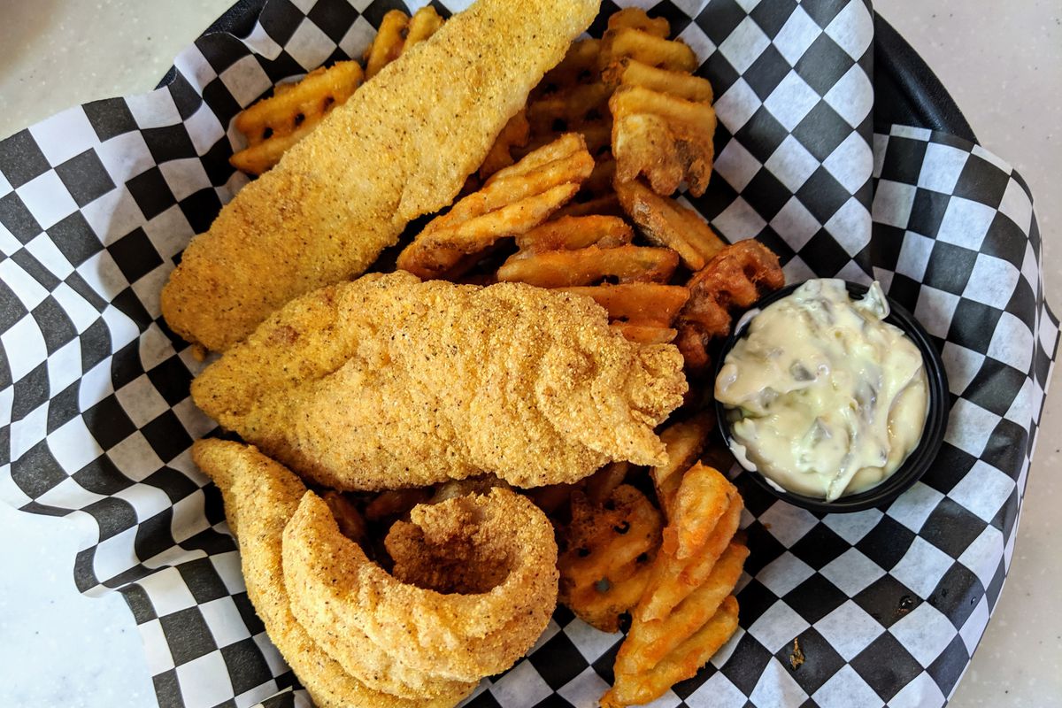 Fried fish with waffles fries under checkered paper basket on a white table.