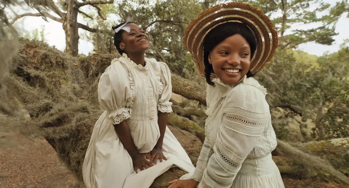 Two teen black girls in 19th-century dresses sitting in a tree.