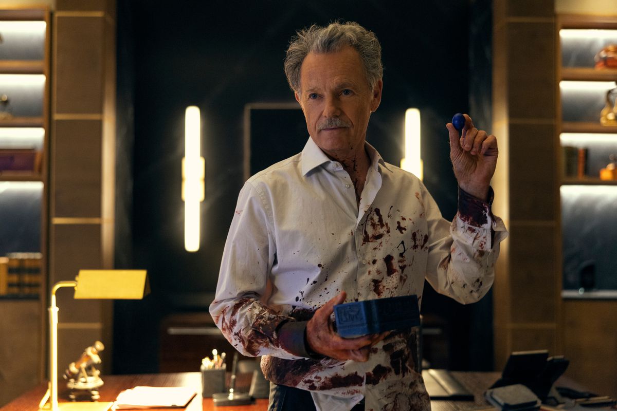 Roderick Usher (Bruce Greenwood) covered in blood holding something small up from a box