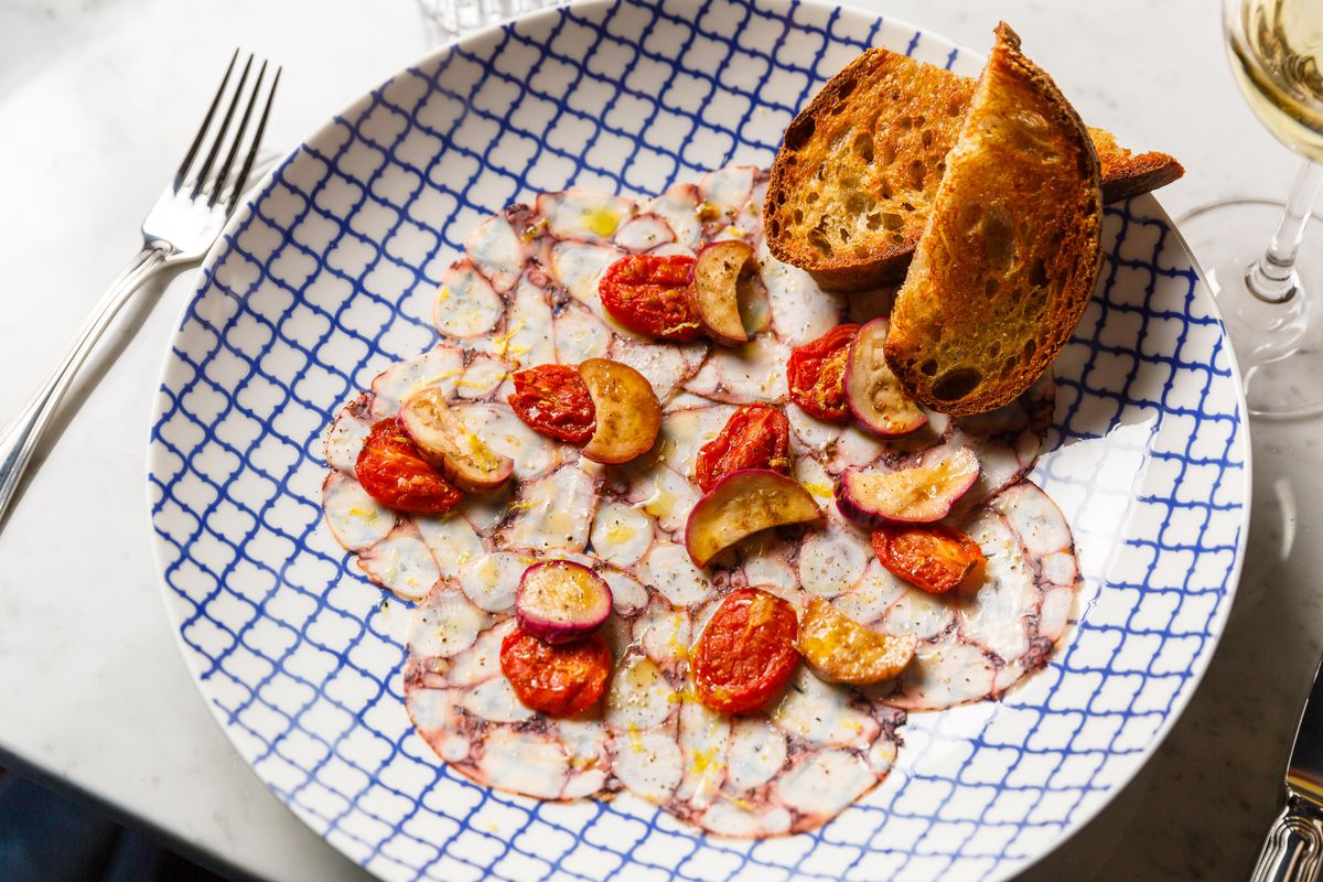 a blue checkered plate with thinly sliced octopus, blistered tomatoes and pieces of thick toast
