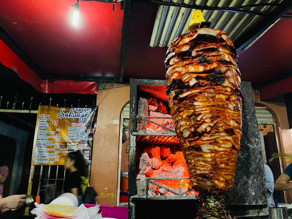 A trompo of meat spins in front of embers. 