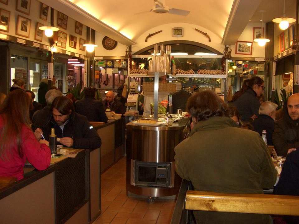A restaurant interior filled with people, with a salad bar in the center, strip lighting beneath a domed ceiling, and pictures and decorations on the walls