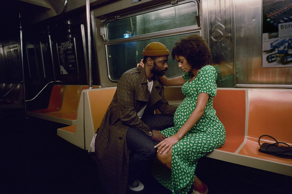 LaKeith Stanfield and Clark Backo sit together on a metro car in The Changeling. Backo is visibly pregnant, and has her arm around Stanfield’s neck, while Stanfield gazes at her with his hand on her lap.