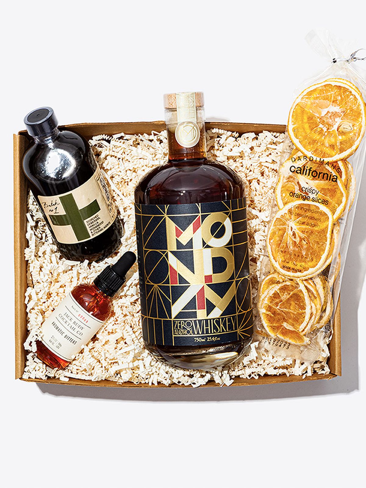 A box with a bottle of Monday non-alcoholic spirit, a bag of dried orange slices, a jar of bitters, and a bottle of old fashioned mix