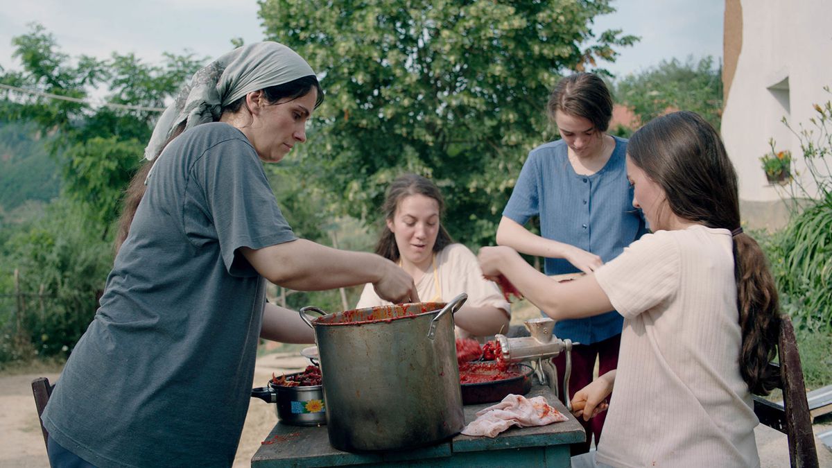 Four women gather around a table with a large pot and a food mill, working.