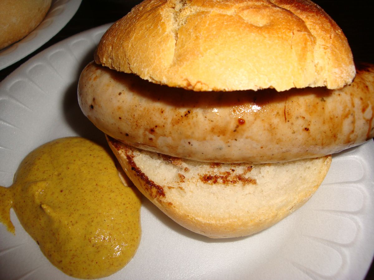 A bratwurst in a kaiser roll with mustard on the side.