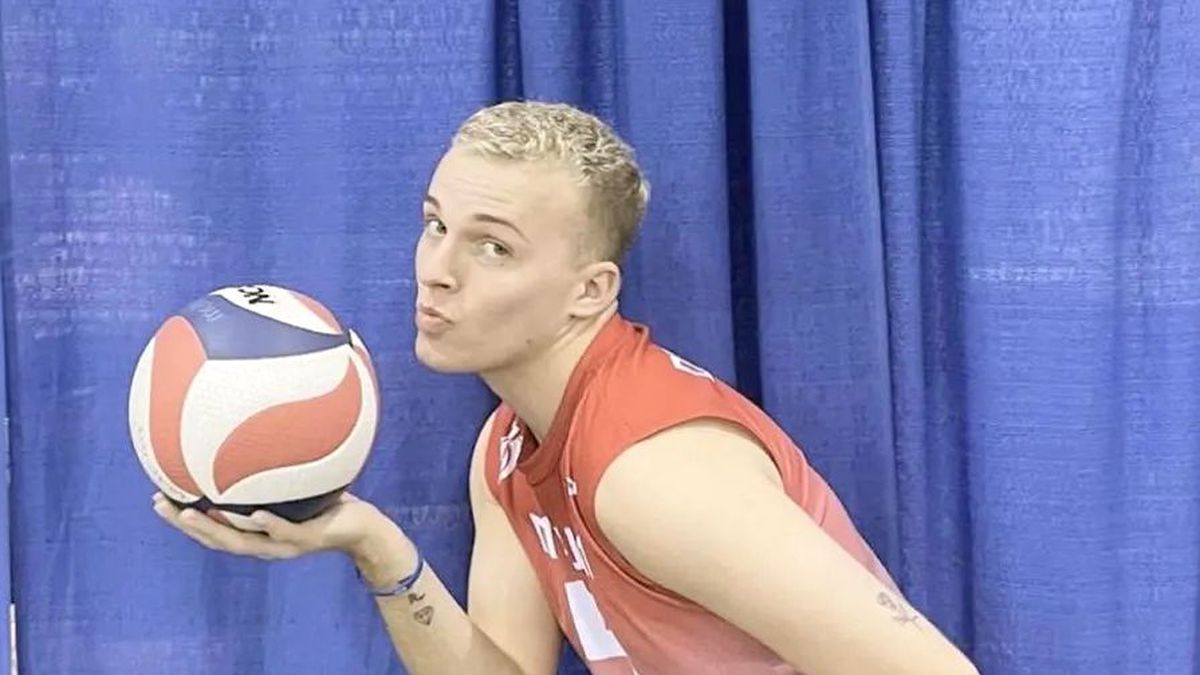 A volleyball player poses with a volleyball while smiling