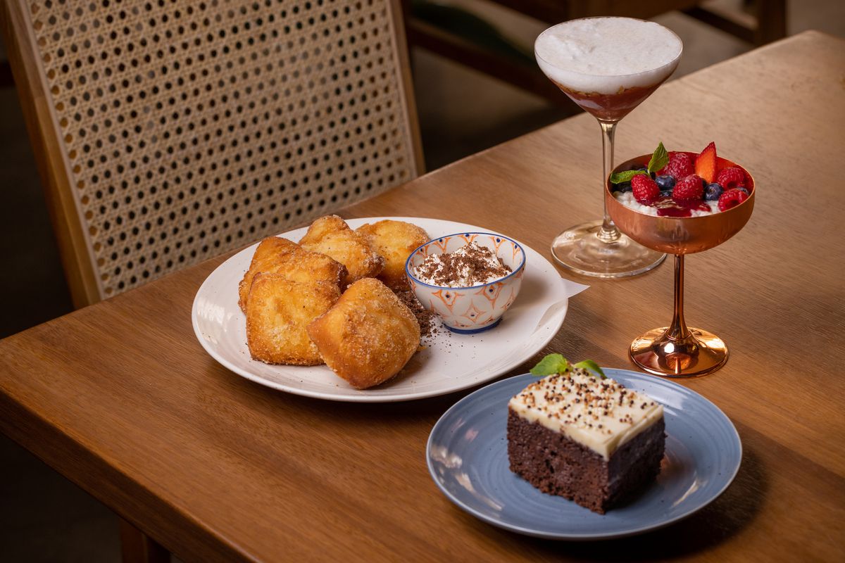 An array of sweets, including fried bread squares, chocolate cake, and drinks.