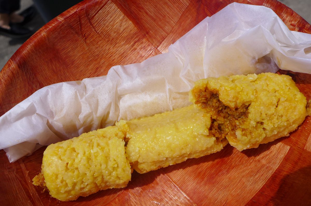 A tamale with a coarse texture yellow dough, broken into thirds.