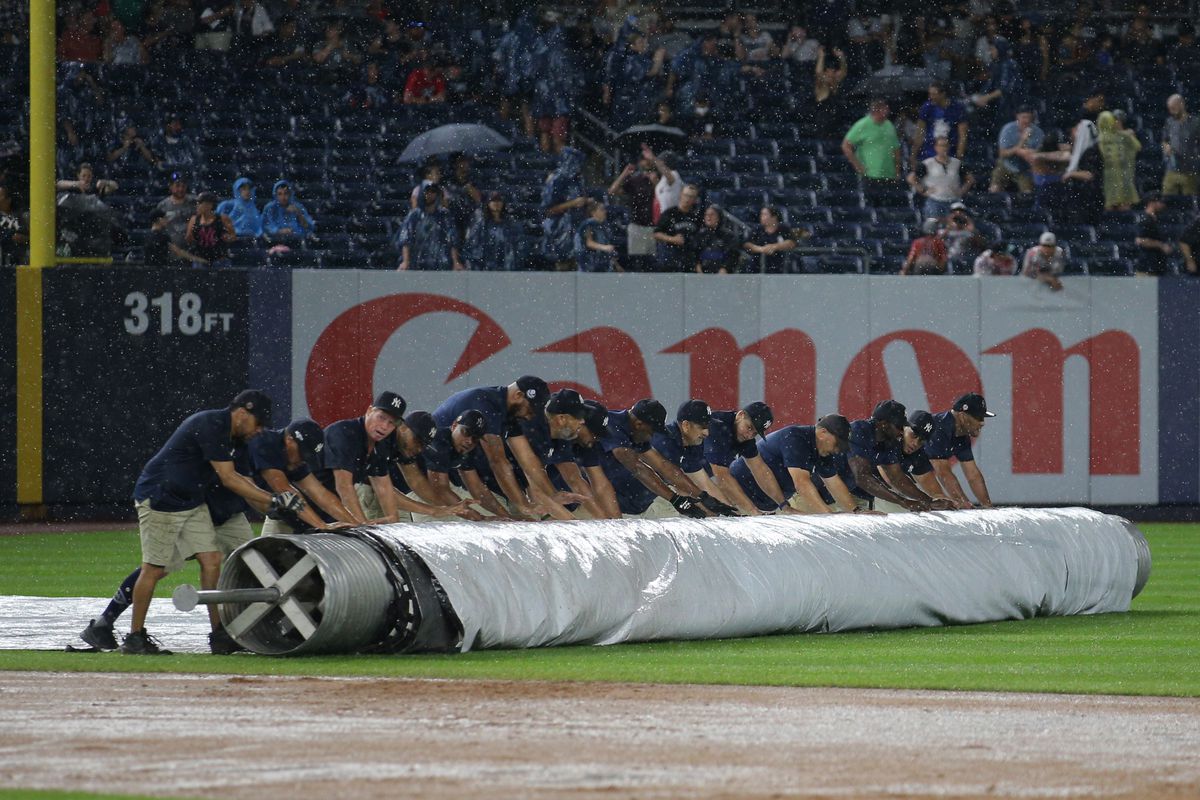 Members of the grounds crew roll the tarp onto the infield during a rain delay during the seventh inning between the New York Yankees and the Boston Red Sox at Yankee Stadium.