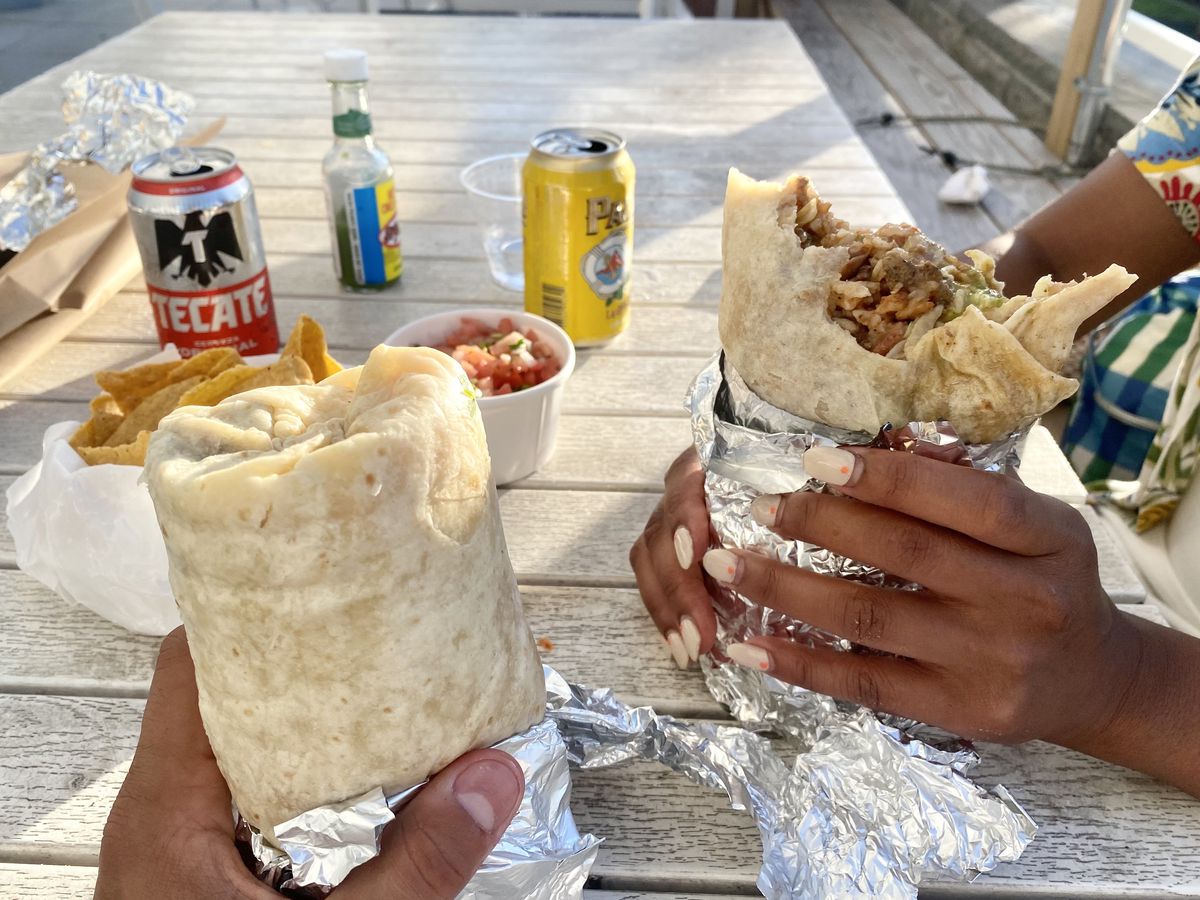 Two hands hold unwrapped burritos.