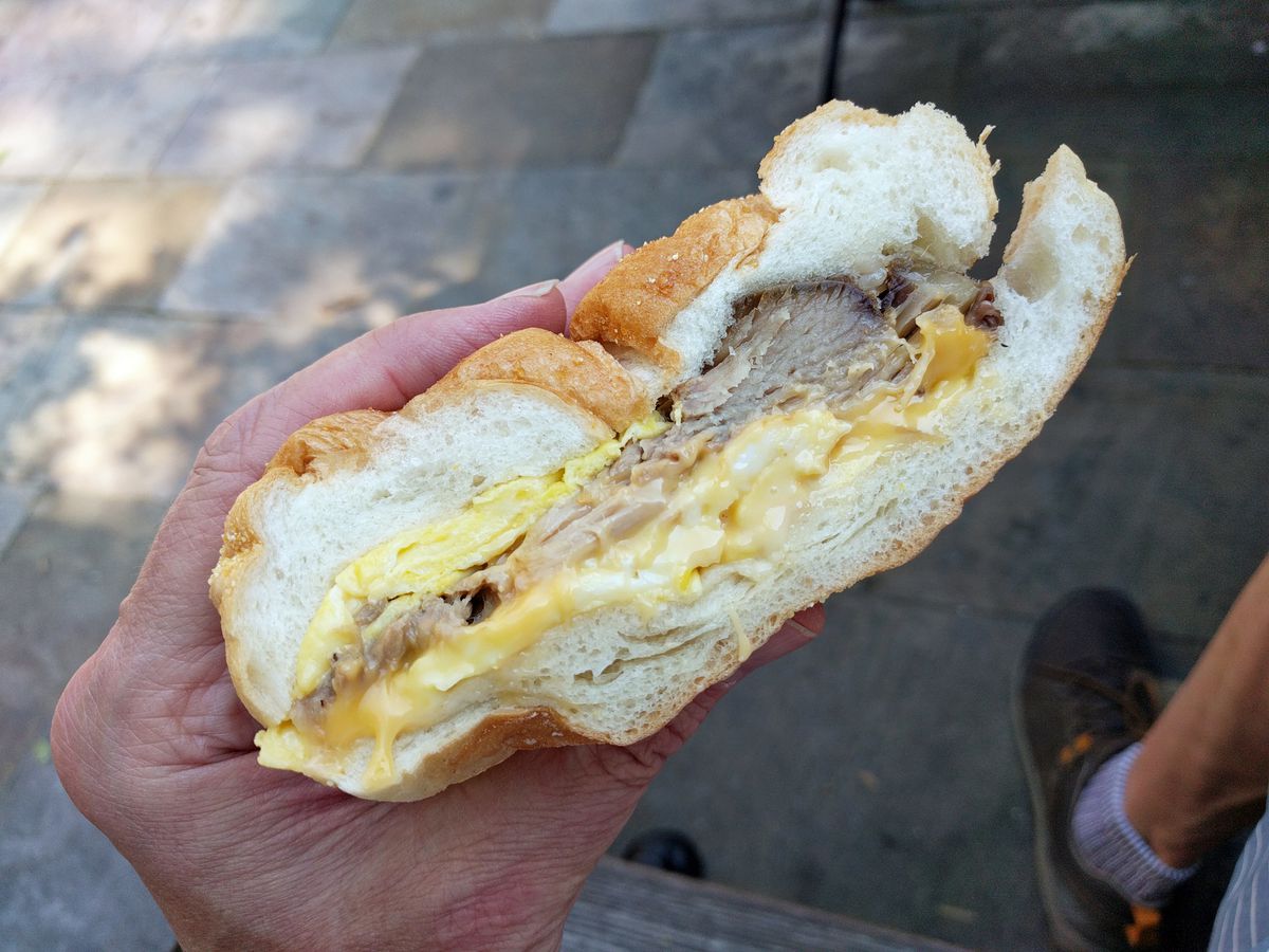 A breakfast sandwich held in hand with pernil, egg, and cheese