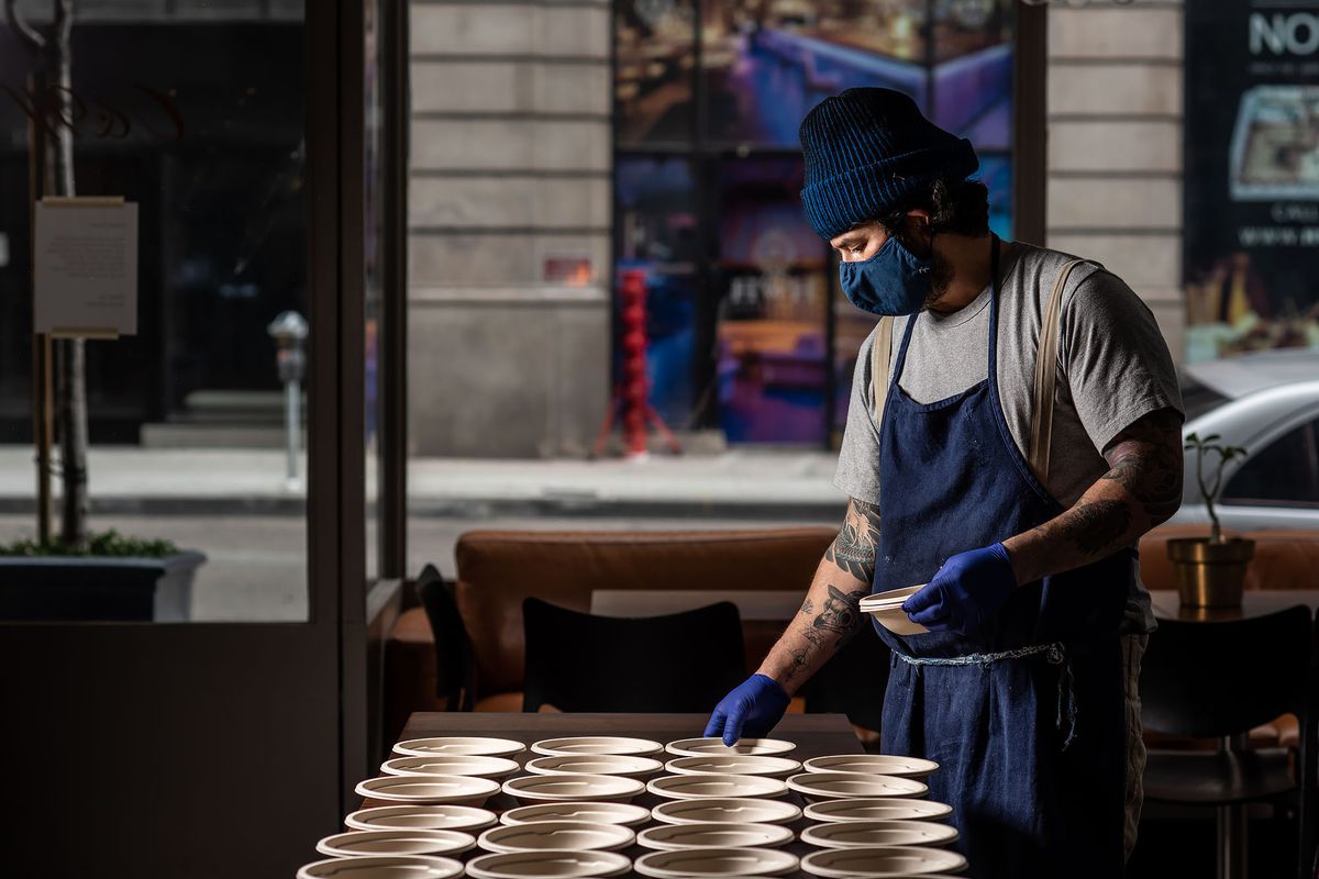 A chef in a blue facemask prepares meals by himself in a closed dining room.