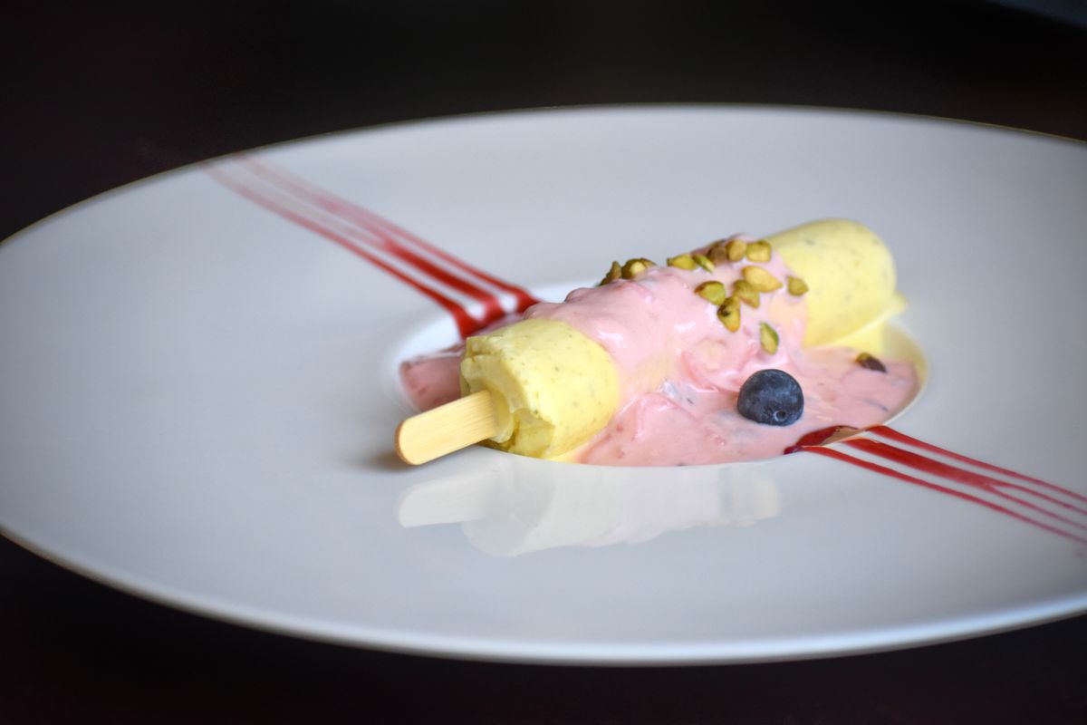 A light pink ice cream on a stick sitting on a white plate.