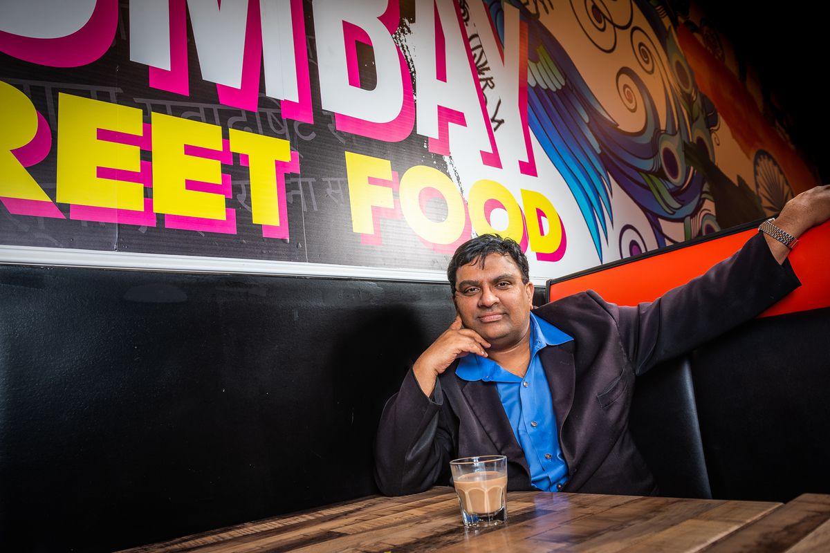 Restaurateur Asad Sheikh sitting in a booth under a mural