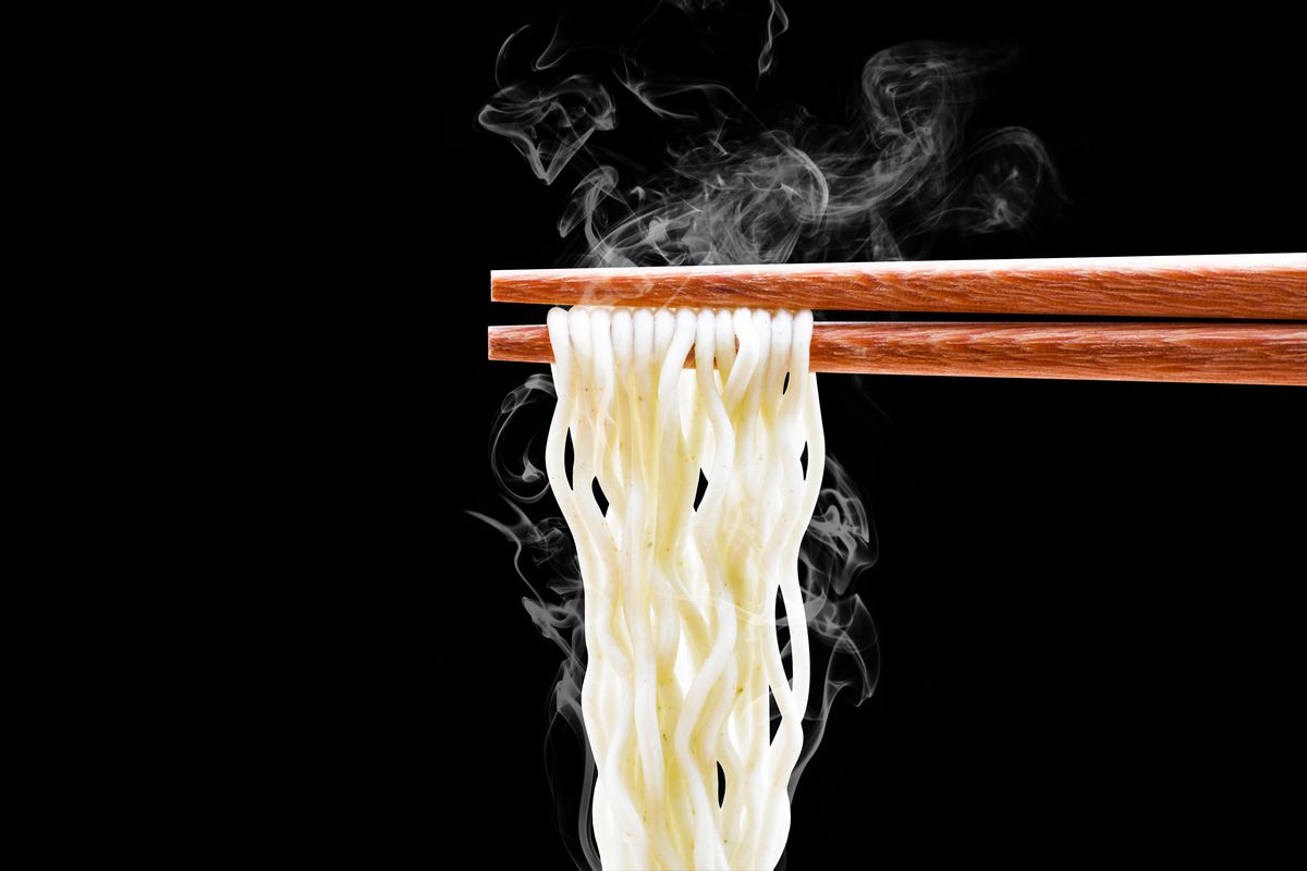 Ramen noodles held up by chopsticks against a black background 