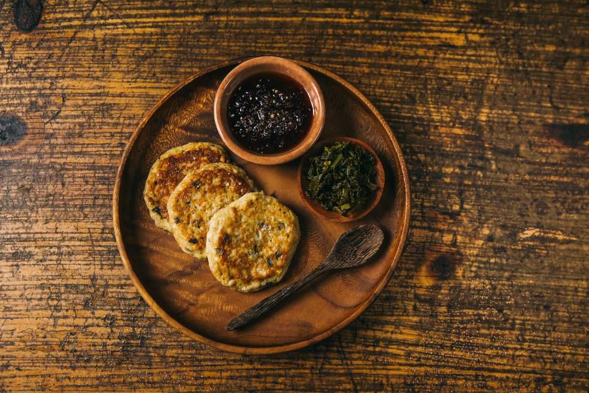 A wooden plate with black-eyed pea pancakes, pepper jam and fermented greens