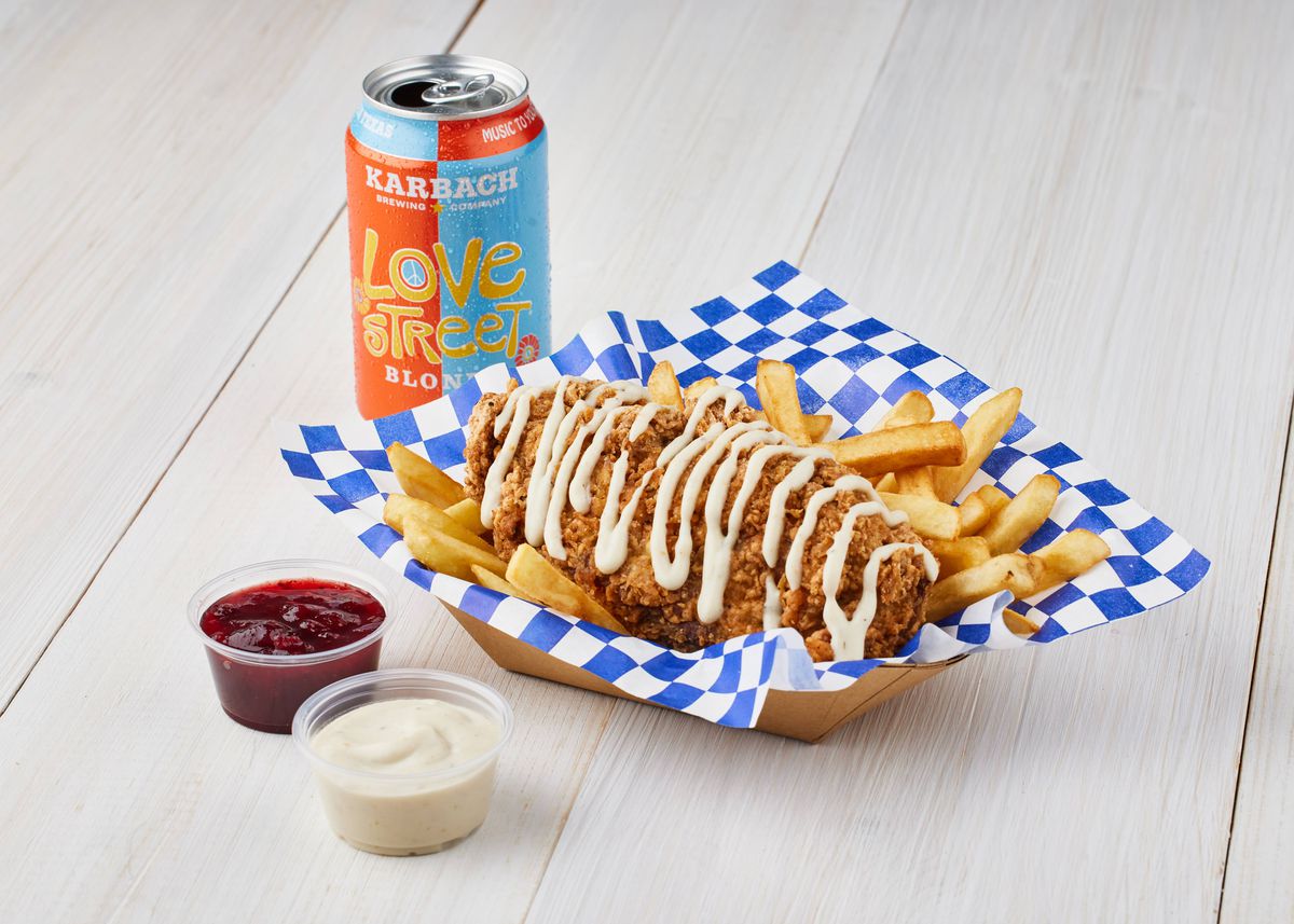 A deep fried turkey rib is coated with sauce and served in a boat with fries. Two dips sit to the left, and a can of beer sits behind.