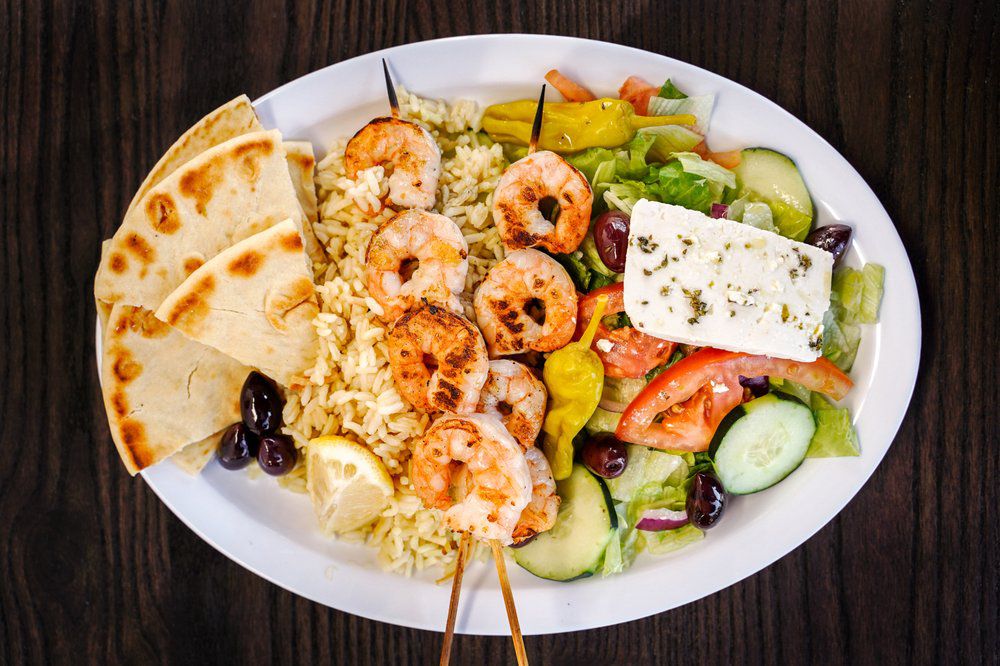 Platter of shrimp skewers, rice, pita bread, and Greek salad.