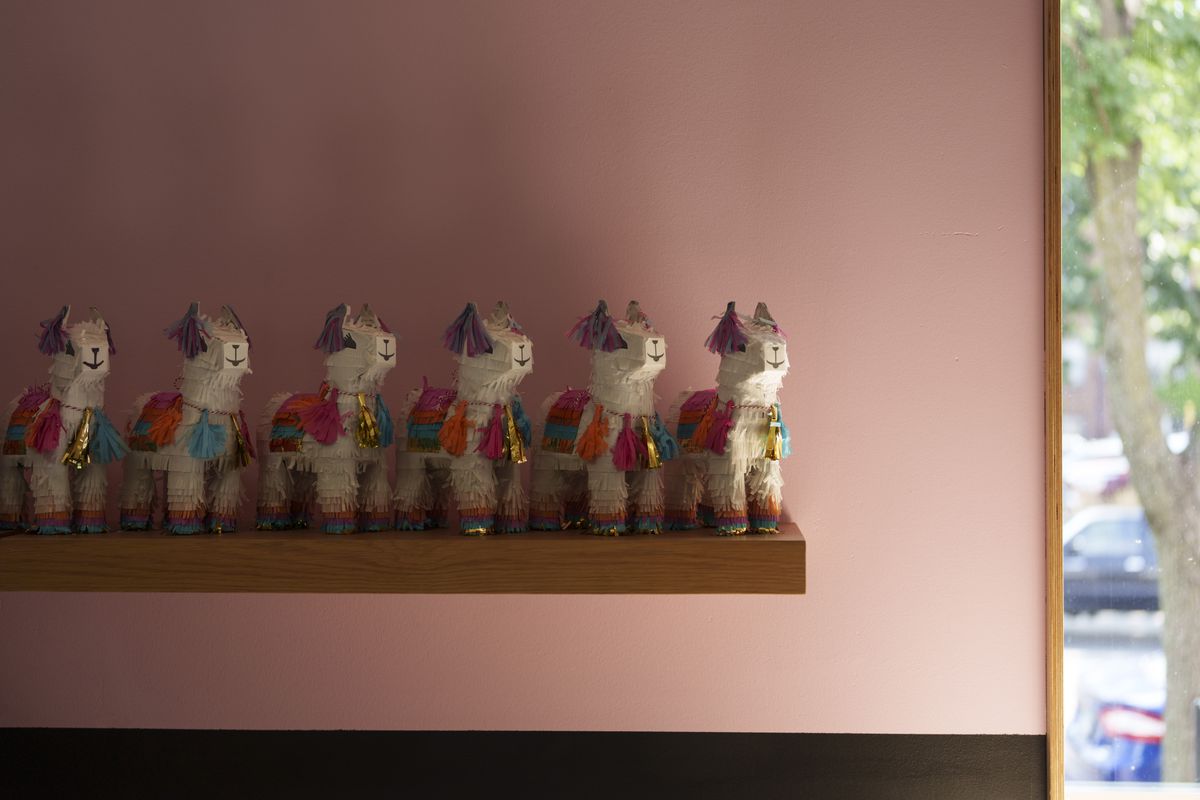 Sculptures of llamas lined up on a shelf against a pink wall. 