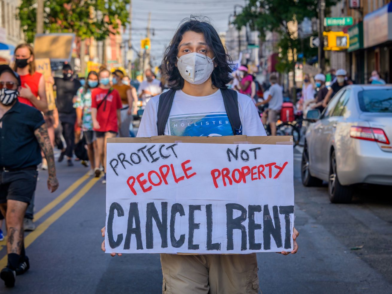 A protester walking down a street carries a sign that reads, “Protect people not property. Cancel rent.”