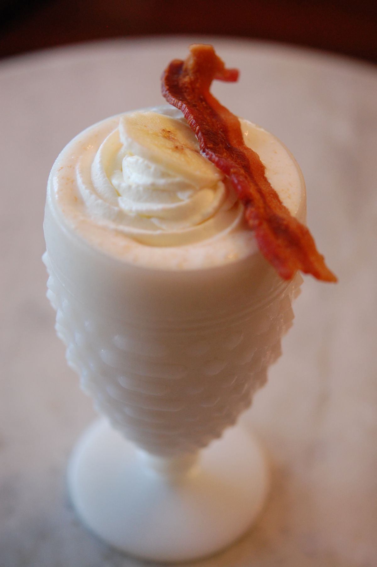 The “Elvis” in a milk glass dish made with banana pudding gelato, peanut butter, bourbon whiskey, vanilla wafers, whipped cream, and bacon
