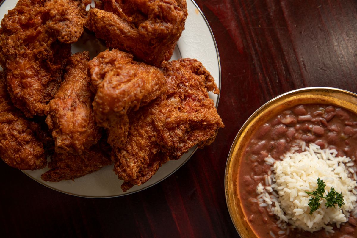A plate of crusty, dark fried chicken next to a bowl of red beans and rice topped with parsley.