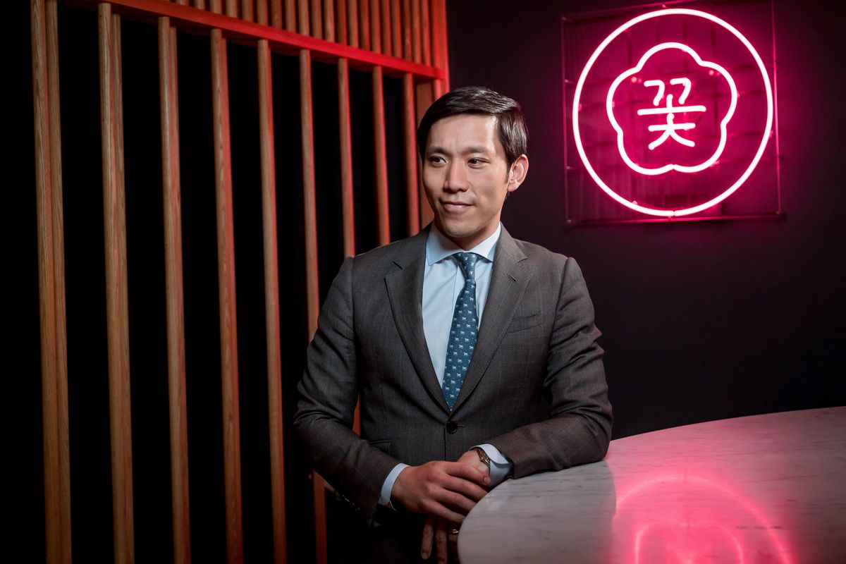 A man, Simon Kim, poses for a photo against an illuminated sign in the background.