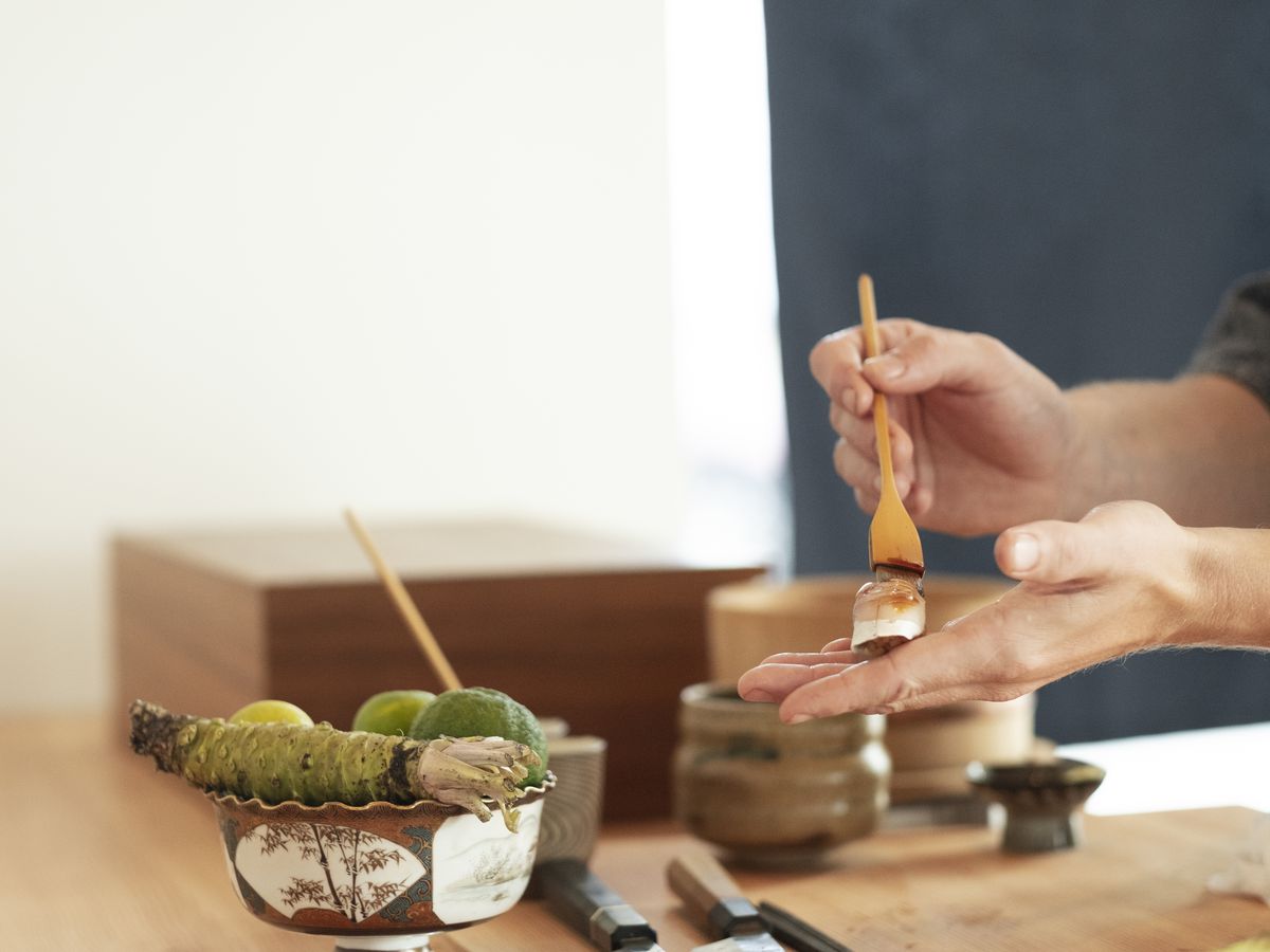 A sushi chef paints a piece of nigiri with sauce. 