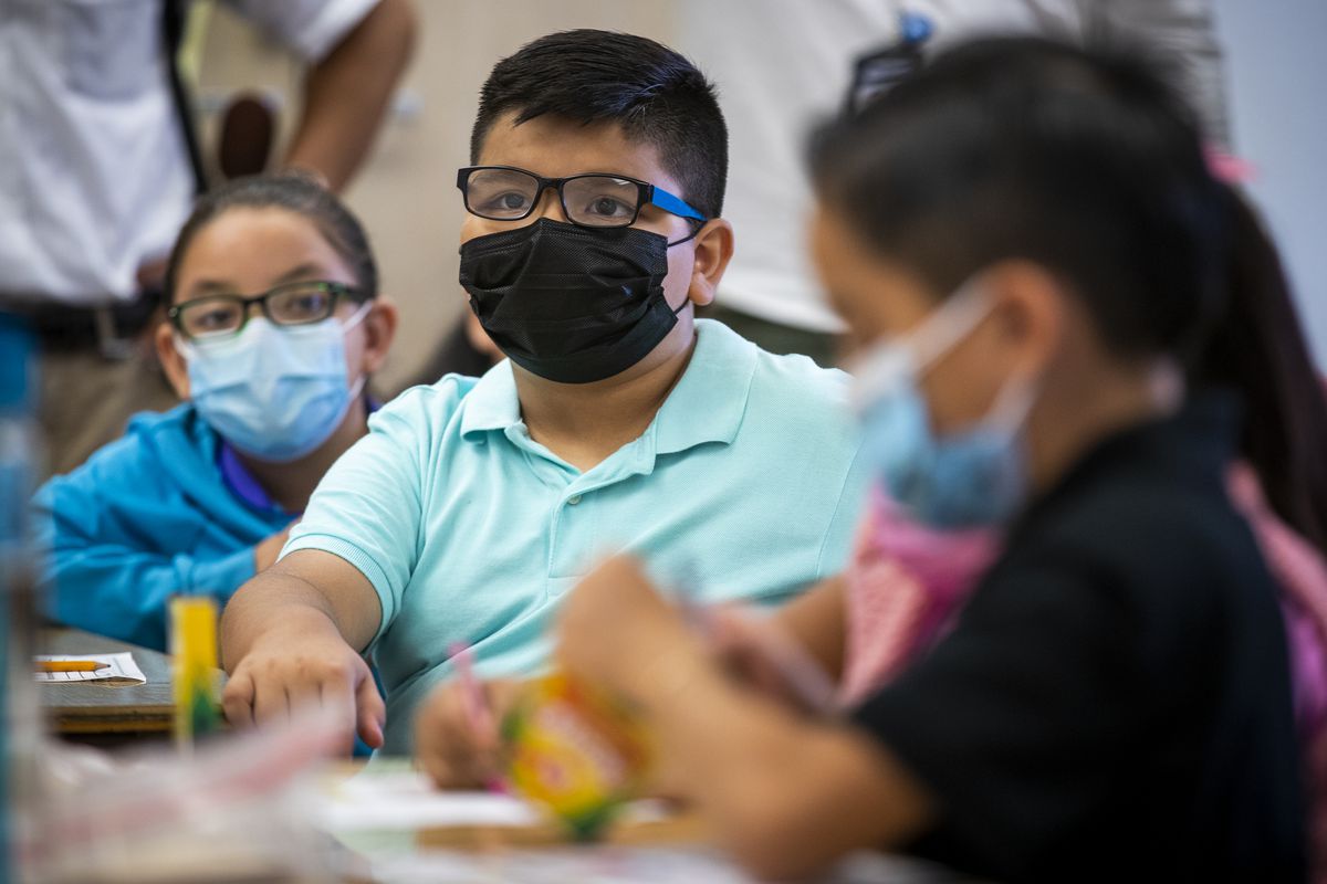 Children wearing masks sit at a classroom table.