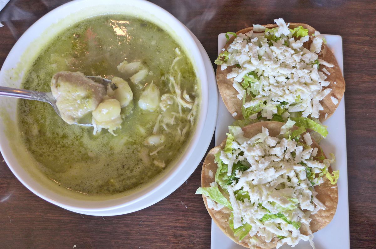 A green soup with a spoonful of chicken and hominy raised above it.